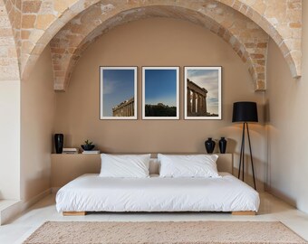 Puede incluir: Tres impresiones enmarcadas de arquitectura griega antigua cuelgan sobre una cama con ropa de cama blanca. La habitación presenta una combinación de colores beige, una arcada de piedra y una lámpara de pie negra. Jarrones negros decorativos y una pequeña planta están en un estante.