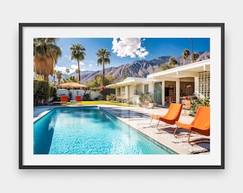 May include: A framed print of a mid-century modern home with a swimming pool. The image features orange lounge chairs, palm trees, and a mountain backdrop under a bright blue sky. The pool's water is a vibrant turquoise color.
