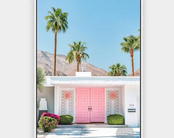 May include: A framed wall art print featuring a mid-century modern house with bright pink double doors, white lattice screens, and the number 504 displayed on the wall. The scene includes palm trees, green bushes, and mountains under a clear blue sky.