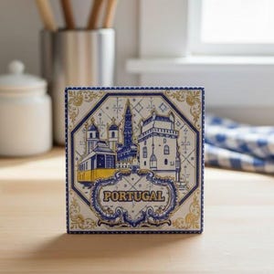 Könnte beinhalten: Quadratische Keramikfliese mit einer blau-gelben Illustration portugiesischer Architektur. Die Fliese hat einen dekorativen Rand und das Wort "PORTUGAL". Die Fliese liegt auf einer Holzoberfläche.
