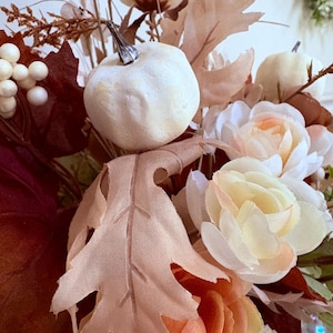 Puede incluir: Arreglo floral oto&ntilde;al con calabazas blancas, rosas color melocot&oacute;n y hojas artificiales en tonos marr&oacute;n y melocot&oacute;n. El arreglo incluye bayas blancas y diversas flores, creando un ambiente c&aacute;lido y acogedor, ideal para decoraci&oacute;n.