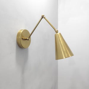 Peut inclure: Applique murale en laiton avec bras réglable et abat-jour conique. L'applique a une base circulaire et un bras pivotant pour un éclairage directionnel. La finition est dorée et métallique.