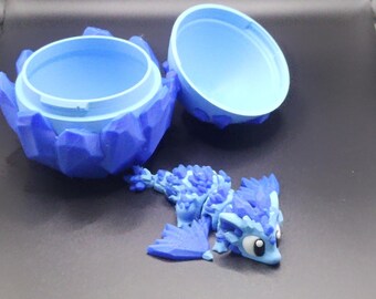 May include: A blue, 3D-printed dragon figurine with a matching egg-shaped container. The container is open, revealing the interior. The dragon is light blue with darker blue accents.