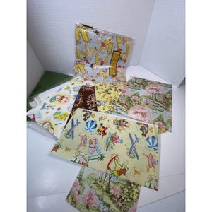 Peut inclure: Une collection de feuilles de papier décoratives assorties présentant divers motifs, notamment des jouets vintage, des avions, des ballons, des paysages floraux avec des arbres roses et des motifs jaunes avec de petites figures, disposées en couches.