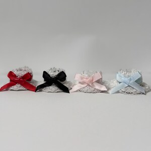 May include: Four lace accessories with satin bows in red, black, pink, and light blue. The lace is white, and the bows are tied in the center of each accessory. The items are arranged in a row against a white background.