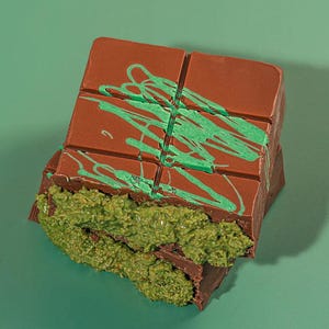 Könnte beinhalten: Eine teilweise zerbrochene Schokoladentafel mit grüner Füllung und grünem Guss obenauf. Die Schokolade hat eine satte braune Farbe, und die Füllung hat ein strukturiertes Aussehen. Der Hintergrund ist einfarbig grün.