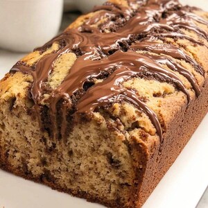 Puede incluir: Un bizcocho de mármol recién horneado con un rico glaseado de chocolate. El bizcocho tiene una base marrón claro con remolinos marrones oscuros y chispas de chocolate. Dos tazas blancas están en el fondo.