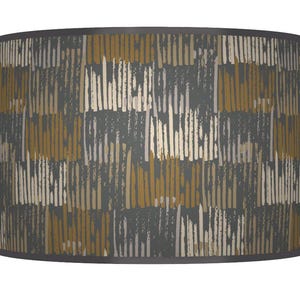 May include: A drum lampshade with a repeating vertical pattern. The design features a dark grey background with mustard yellow, beige, and off-white brushstroke-like lines. The top and bottom edges are trimmed with a dark grey band.