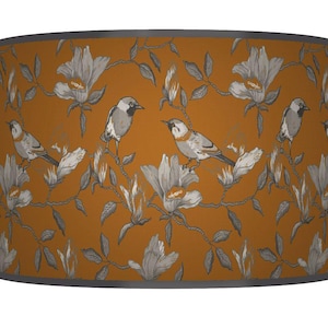 May include: Mustard-yellow lampshade with a repeating pattern of grey birds, flowers, and foliage. The lampshade has a grey trim along the top and bottom edges. The design is a botanical theme.