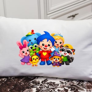 May include: A rectangular white pillow featuring a colorful graphic print of a group of cartoon characters, including a central figure with blue hair and a red outfit, surrounded by a pink rabbit, a blue elephant, a green frog, and other animals.