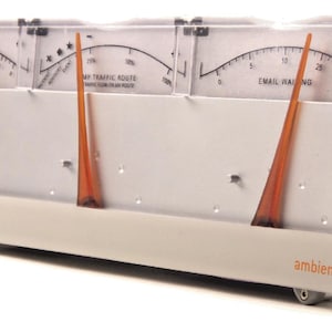 May include: A cream-coloured electronic device with three gauges, each featuring an orange needle and a curved scale. The device has a clear plastic cover and the word "ambient" is printed on the front. The gauges display text related to traffic and email.