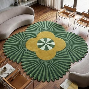 May include: A large, circular area rug featuring a central yellow four-petaled flower motif with a green and white striped center, surrounded by radiating dark green fan-shaped petals, positioned on a dark wood floor in a living room.