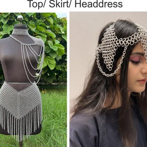 Puede incluir: Un conjunto de top, falda y tocado de cota de malla plateada. El top presenta un choker y una ca&iacute;da en el hombro con cadenas colgantes. La falda tiene un dobladillo con flecos. El tocado lo lleva una persona con pelo largo y oscuro.