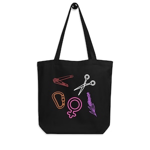 May include: Black tote bag with a variety of colorful line art illustrations. The illustrations include nail clippers, scissors, a carabiner, a female symbol, and a sprig of lavender. The bag has two black handles and a black interior.