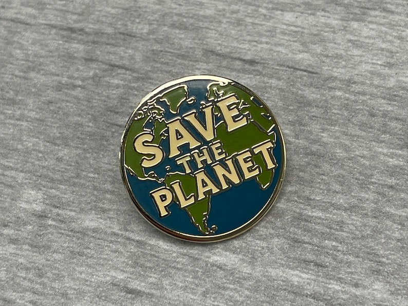 以下が含まれることがあります： 金色の縁取りと「SAVE THE PLANET」の文字が金色で書かれた丸いエナメルピン。青と緑の世界地図のデザインで、環境意識を促進しています。