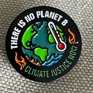 May include: Round black enamel pin with the text "THERE IS NO PLANET B" in white. The pin features a green and blue Earth with a thermometer and flames, and the words "CLIMATE JUSTICE NOW".