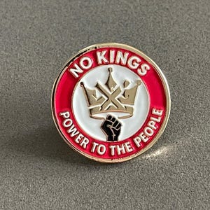 May include: Round enamel pin with a gold border and the words "NO KINGS" and "POWER TO THE PEOPLE" in white lettering on a red background. A gold crown and a black fist are in the center.