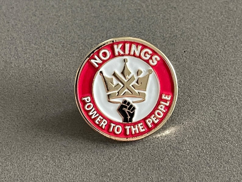 May include: Round enamel pin with a gold border and the words "NO KINGS" and "POWER TO THE PEOPLE" in white lettering on a red background. A gold crown and a black fist are in the center.