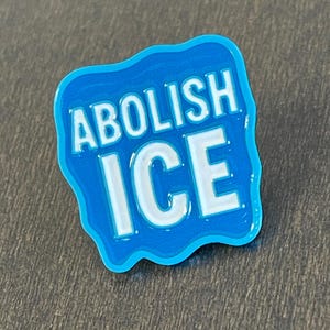 K&ouml;nnte beinhalten: Ein blauer Emaille-Pin mit den Worten "ABOLISH ICE" in wei&szlig;en Blockbuchstaben. Der Pin hat einen hellblauen Rand und eine wellenf&ouml;rmige Form und ist wahrscheinlich ein politisches Statement oder ein Protestartikel.