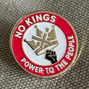 May include: Round pin with a red border and gold trim. The pin features the text "NO KINGS" and "POWER TO THE PEOPLE" in white. A gold crown design and a black fist are in the center.