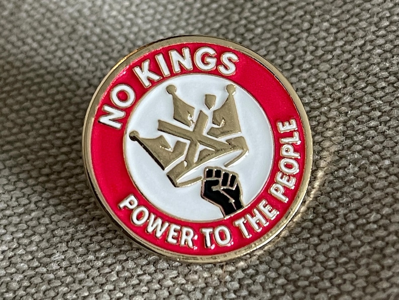 May include: Round pin with a red border and gold trim. The pin features the text "NO KINGS" and "POWER TO THE PEOPLE" in white. A gold crown design and a black fist are in the center.