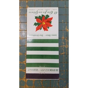 May include: A vintage matchbook with a red poinsettia flower and green leaves on a white background. The text "A Lure for an Epicure" is above the flower. The matchbook has green and white stripes and the text "30 STICK MATCH BOOK".