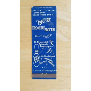 May include: A vintage matchbook from Blue Ridge Bowl in Kansas City, Missouri. The blue matchbook features the bowling alley's name, address, and services, including a snack bar and pro shop. The design includes a bowling pin graphic and the text "Air Conditioned".