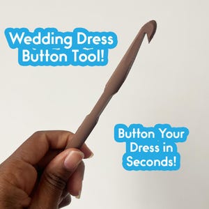 Peut inclure: Un outil marron pour boutonner une robe de mariée, avec une extrémité en forme de crochet. L'outil est tenu dans une main sur fond blanc. Le texte de l'image indique "Wedding Dress Button Tool!" et "Button Your Dress in Seconds!"