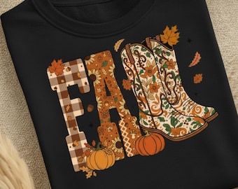 Può includere: Felpa nera con la scritta "FALL" in un design a tema autunnale. La "F" ha un motivo a quadri marrone, la "A" ha girasoli e la "L" ha stivali da cowboy con motivi floreali. Le zucche e le foglie completano il design.