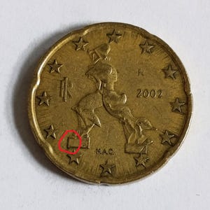 May include: A gold-coloured 2002 Italian 50 Euro cent coin. The coin features a depiction of Italy, surrounded by stars, with the year 2002 visible. The coin has the letter "R" and the initials "M.A.C."
