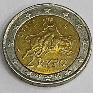 May include: A two-euro coin with a gold center and silver outer ring. The gold center features a depiction of a woman riding a bull, with the text "2 EYPΩ" and the year "2002". The outer ring has star-shaped designs.