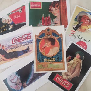 May include: A collection of seven rectangular postcards featuring vintage Coca-Cola advertisements. The prints display various illustrations of people drinking soda, including text such as Drink Coca-Cola, Delicious and Refreshing, New cooler for Coke, and Play Refreshed, all rendered in classic red, white, and gold colour palettes.