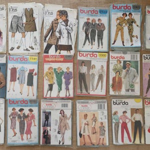 May include: A collection of eighteen Burda sewing pattern envelopes arranged in three rows. Each envelope features illustrations of clothing designs, including dresses, trousers, jackets, and skirts, with brand logos and model numbers printed on each.