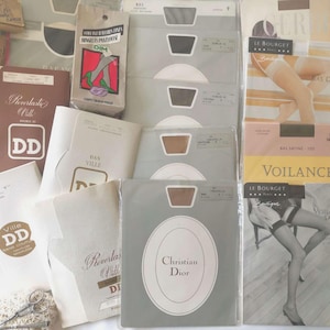 Può includere: Una collezione di confezioni di calze vintage che include vari marchi come Christian Dior, Le Bourget e DIM. L'assortimento presenta buste di carta rettangolari e calze avvolte nella plastica in toni neutri, con loghi e testi dei marchi.