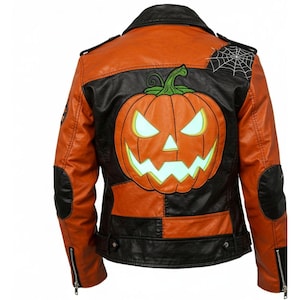 Op de afbeelding: Oranje en zwarte Halloween-jas. De achterkant heeft een groot geborduurd jack-o'-lantern met gloeiende ogen en een spinnenweb patch. De jas heeft een klassieke biker-stijl met een ritssluiting en gewatteerde schouders.