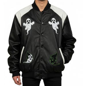 May include: Black and white varsity jacket with ghost patches. The jacket features a black body, white sleeves, and a black collar and cuffs. Three white ghost patches and one green ghost patch are sewn onto the jacket.