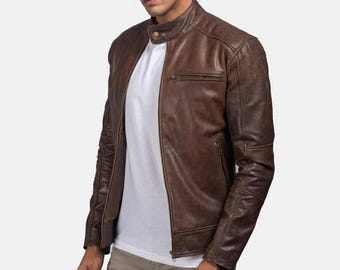 May include: A brown leather jacket with a stand-up collar and a front zipper. The jacket has a classic design with a chest pocket and quilted detailing on the shoulders and sleeves. The jacket is worn over a white t-shirt.
