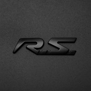 Op de afbeelding: Een matzwarte embleem met de letters "RS" in een gestileerd lettertype. Het embleem staat tegen een getextureerde, donkergrijze achtergrond, wat een contrast creëert dat het ontwerp benadrukt. De letters zijn verbonden door kleine rechthoeken.