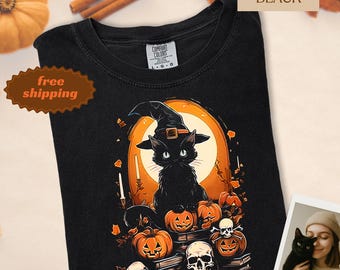 May include: Black t-shirt featuring a Halloween-themed graphic. The design includes a black cat wearing a witch hat, surrounded by pumpkins, skulls, and candles. The shirt has the text "Comfort Colors" on the tag.