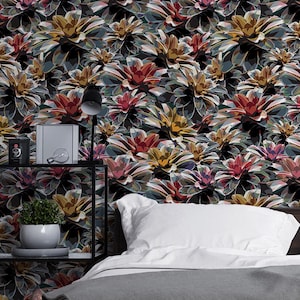 May include: A bedroom scene featuring a floral wallpaper with a repeating pattern of colorful, stylized flowers in shades of red, yellow, and purple against a dark background. The room includes a bed with white linens, a gray blanket, and a black metal shelf with decorative items.