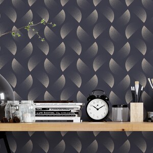 Könnte beinhalten: Ein Heimbüro mit dunkelblauer Tapete mit einem sich wiederholenden abstrakten Muster. Ein Holztisch beherbergt eine schwarze Vase mit einem Zweig, einen Wecker und Kunstbedarf. Ein Metallhocker und ein Drahtkorb vervollständigen die Szene.