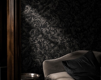 May include: A dark wallpaper featuring a repeating black and charcoal gray damask pattern with intricate swirling acanthus leaf motifs. The wall is partially illuminated by a light source, highlighting the texture of the ornate floral design.