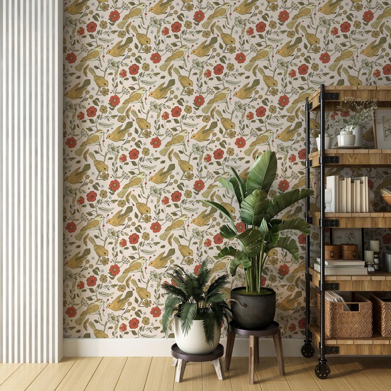 May include: Wallpaper featuring a repeating pattern of yellow birds, red flowers, and green leaves on a cream background. The design is displayed on a wall behind a wooden shelving unit with black metal frames and two potted green plants.