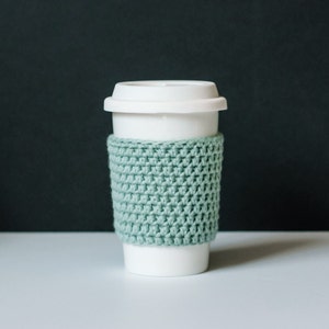 May include: A white ceramic travel mug with a light green crocheted cosy.