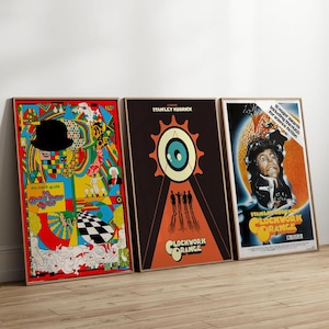 May include: Three framed movie posters. The posters feature colorful graphics and text, including "Clockwork Orange" and "Stanley Kubrick." The posters are displayed against a light-colored wall.