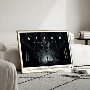 Puede incluir: Póster enmarcado de la película "Alien: Romulus". El póster presenta una criatura alienígena amenazante con el título en la parte superior. Una figura se encuentra en una puerta iluminada. El póster está en un marco dorado y descansa sobre una alfombra estampada.
