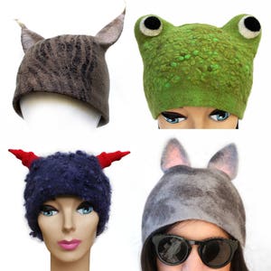 Puede incluir: Cuatro sombreros de lana fieltro con orejas de animales. Los sombreros son de varios colores, incluyendo gris, marrón, verde y azul. Cada sombrero tiene características animales únicas, como orejas de gato, ojos de rana y cuernos de diablo.