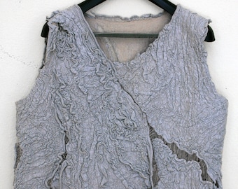 May include: A gray sleeveless vest made of crinkled fabric with a textured surface. The vest has a V-neck and a loose, flowing fit.