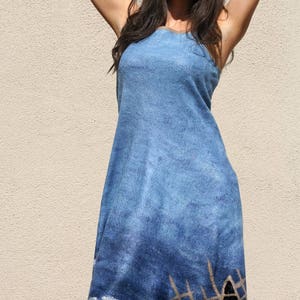 May include: A woman wearing a blue denim dress with a silver and brown fish net design. The dress has a loose fit and a sleeveless design. The woman is wearing sunglasses and smiling.