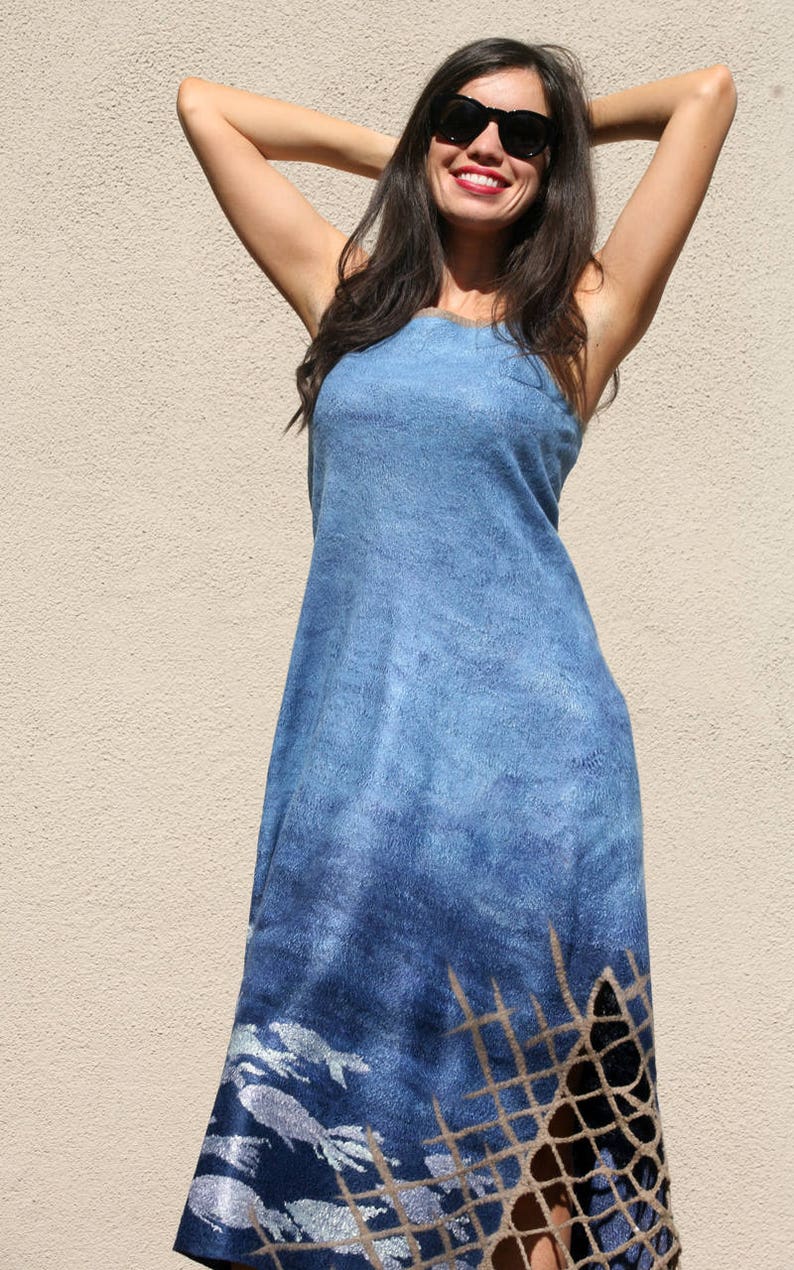 May include: A woman wearing a blue denim dress with a silver and brown fish net design. The dress has a loose fit and a sleeveless design. The woman is wearing sunglasses and smiling.